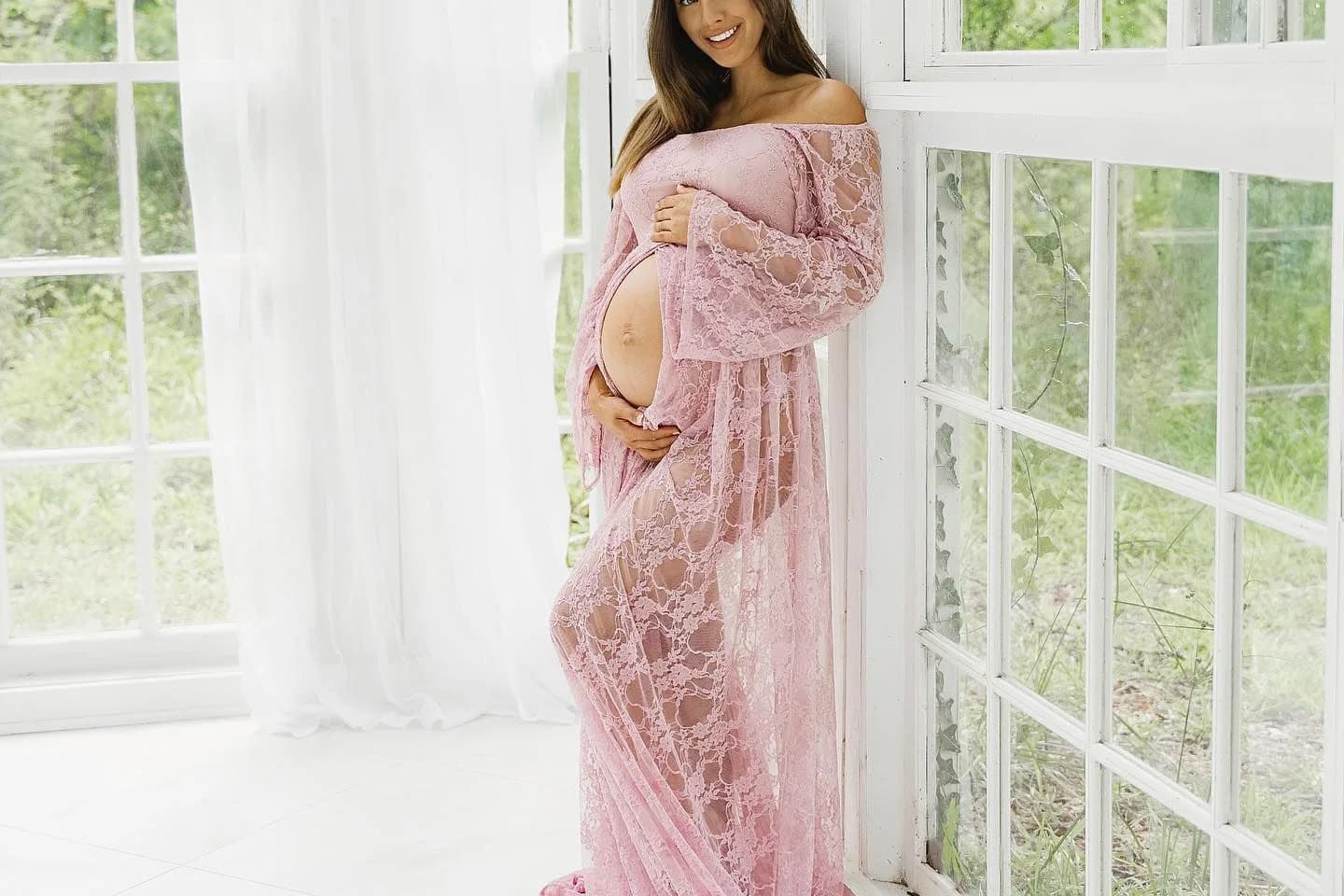 April in a pink lace maternity gown by a window